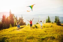 Three Kids In The Mountains At Sunset Play Kite And Butterfly Fishing Net. Happy Summer Holidays And Childhood.