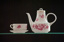 White Teapot And A Cup Of Tea With Beautiful Red Flowers On A Black Background