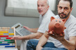 © Giulio_Fornasar - Man showing a piggy bank while his senior father is calculating