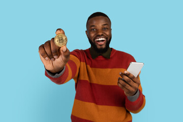 Poster - Online Trading. Excited Young Black Man Holding Golden Bitcoin And Smartphone