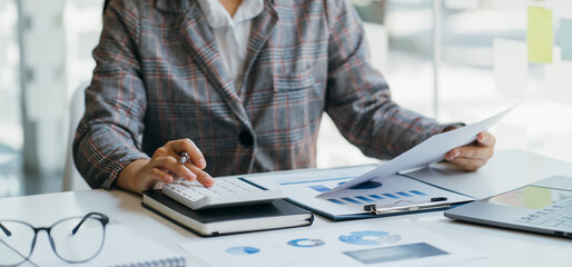 Female director working in office sitting at desk analyzing business statistics holding diagrams and charts using laptop