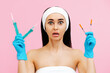 © _KUBE_ - Portrait of a shocked young woman with surgical markings on her face, holding syringes in her hands. Pink background. Concept of a victim of plastic surgery