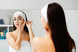 © _KUBE_ - A young beautiful woman looks in the mirror and adjusts the bandage on her head to begin beauty procedures. Skin care and beauty routine concept
