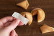 Person holds in hand blank paper slip from fortune cookie against few cookies laying on table surface background, mockup for your good luck wish