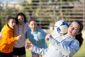 Happy school girls having fun with ball on stadium. Team of four joyous girlfriends preparing for football game training to win and demonstrating skills. Healthy lifestyle, leisure, team sport concept