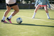 Sporty girls passing football ball on green field. Two young girls in sportswear playing football together, running fast and professionally kicking ball. Healthy lifestyle and womens football concept