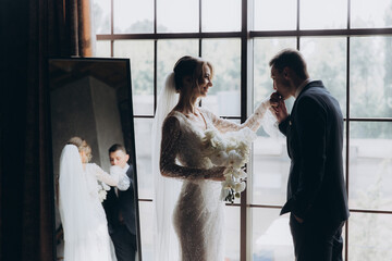 Wall Mural - The first meeting of the groom in a black suit and the bride in a white wedding dress with a bouquet in the interior of a photo studio, hotel, on black background