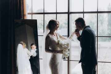 Wall Mural - The first meeting of the groom in a black suit and the bride in a white wedding dress with a bouquet in the interior of a photo studio, hotel, on black background