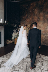 Wall Mural - The first meeting of the groom in a black suit and the bride in a white wedding dress with a bouquet in the interior of a photo studio, hotel, on black background