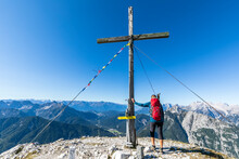 Female Hiker Touching Summit Cross Of Brunnensteinspitze