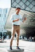 Smiling Businessman Using Tablet PC Standing On Seat Outside Modern Building
