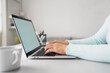 © Suradech - Women using laptop with blank screen at table in the office, Back view of business women hands busy using laptop at office desk.