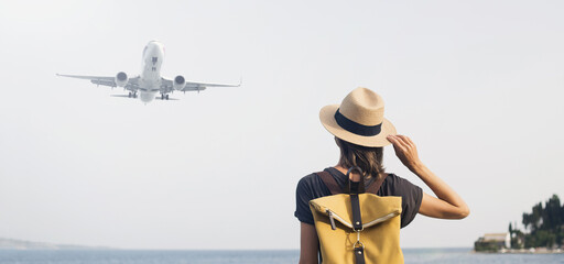 Wall Mural - Young woman looking at plane flying above the sea panoramic banner. Travel, tourism, transportation, enjoy life and active lifestyle concept.