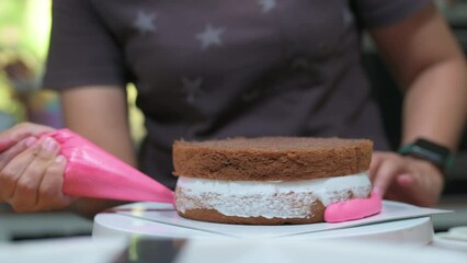 Sticker - A woman spreads cream on top of the cake layers.Decorating pink cake with fresh strawberries pieces.