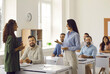 © Studio Romantic - Group of adult students having discussion with business coach during course training class in modern classroom. Woman stands up and speaks out while colleagues are sitting at tables and listening