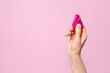 Mature content A young woman folding a pink menstrual cup in her hand. Pink colored background. Space for text. Eco-friendly silicone women's health cycle