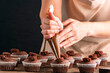 Pastry-cook hand prepare chocolate cupcakes. Woman decorates muffins with chocolate cream on kitchen.