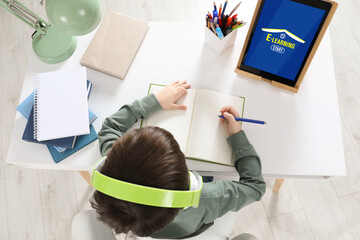 Wall Mural - Cute little boy with modern tablet studying online at home, top view. E-learning