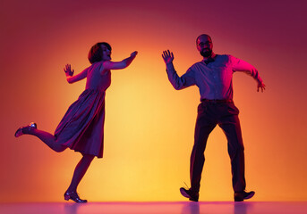 Wall Mural - Portrait of excited man and woman, couple of dancers in vintage retro style outfits dancing lindy hop dance isolated on gradient yellow and purple background.