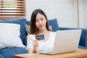 Wall Mural - Young asian woman sit on sofa using laptop computer shopping online with credit card buying to internet, happy girl payment with e-business on couch, purchase and payment, business concept.