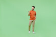 Full body young smiling happy fun man 20s wear casual orange t-shirt hold in hand use mobile cell phone isolated on plain pastel light green color background studio portrait. People lifestyle concept.