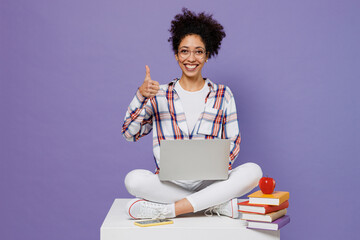 Wall Mural - Full body young girl woman of African American ethnicity teen student in shirt hold use work on laptop pc computer show thumb up isolated on plain purple background. Education in university concept.