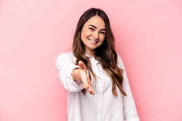 Young caucasian woman isolated on pink background stretching hand at camera in greeting gesture.