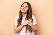 © Asier - Young caucasian woman isolated on beige background has friendly expression, pressing palm to chest. Love concept.