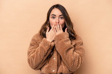 Wall Mural - Young caucasian woman isolated on beige background shocked, covering mouth with hands, anxious to discover something new.