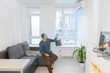 © Angelov - Young Man On Sofa Operating Air Conditioner With Remote Control.