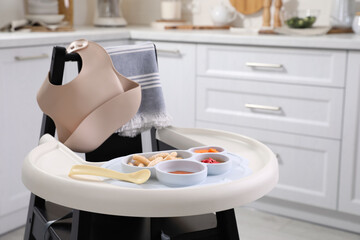 Canvas Print - High chair with food in baby tableware on tray indoors