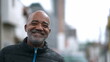 A happy senior black man portrait face smiling at camera standing outside in street