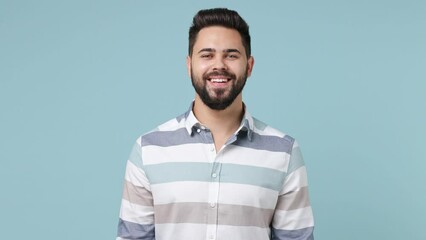 Cheerful fun young bearded brunet man 20s years old wears striped shirt looking camera nodding smiling isolated on plain pastel light blue background studio portrait. People emotions lifestyle concept