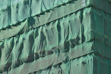 A Building Under Construction Wrapped Green Protection Safety Net.