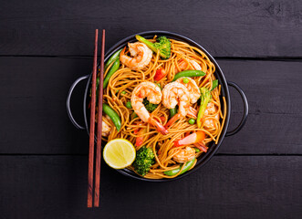 Poster - Stir-fried spaghetti or stir-fry noodles with vegetables and shrimp in a black bowl. dark background, top view