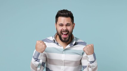 Wall Mural - Excited jubilant overjoyed fun young bearded brunet man 20s wears striped shirt doing winner gesture celebrate clenching fists say yes isolated on plain pastel light blue background studio portrait