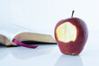 Red bitten apple with an open Holy Bible Book on white background. The Christian biblical concept of the biblical story in Genesis of forbidden fruit, temptation, and disobedience to God. A closeup.
