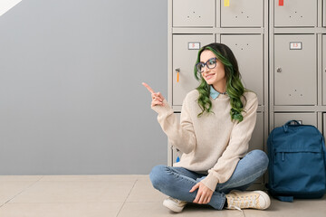 Canvas Print - Beautiful female student pointing at something while sitting near locker at the university