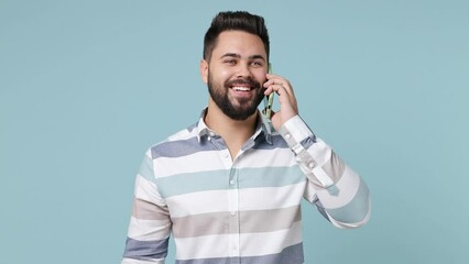 Wall Mural - Cheerful happy calm young bearded brunet man 20s wears striped shirt hold use talk on mobile cell phone conducting pleasant conversation isolated on plain pastel light blue background studio portrait