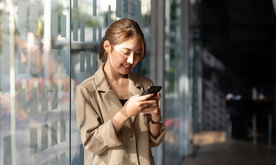 Wall Mural - Happy young smiling Asian woman standing using a mobile phone