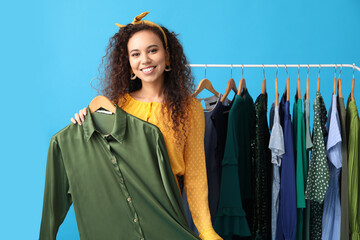 Wall Mural - Beautiful African-American girl near rack with clothes for high school prom on blue background