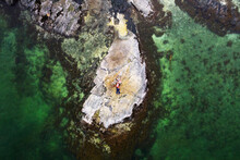 Aerial View Of Family Lying On Rock Surrounded By Clear Green Water