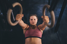 Portrait Of Caucasian Female Athlete Performing Pull-up On Gymnastic Rings, Motivated Fit Girl With Strong Body Exercising In Gym Studio - Health Power And Endurance Competition In Sport