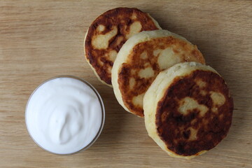 Sticker - Breakfast three cheesecake cheese pancakes lie on a wooden tray table next to a white sour cream sauce. healthy proper nutrition Russian breakfast. cottage cheese dishes