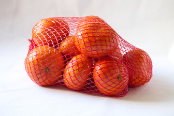 a group of tropical fruit orange mandarin, clementine, tangerine in a red mesh bag packing on white background.