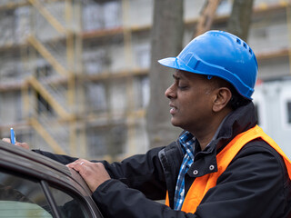 Canvas Print - Indian engineer wearing protective workwear checking his projects and signing documents, outdoors