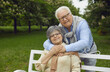 © Studio Romantic - Elderly happy man and woman are resting in the park on a bench, breathing fresh air, a man standing behind and holding his spouse, happy family life, outdoor recreation.