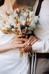 Wall Mural - The bride and groom holds in her hands a beautiful bouquet of dried flowers in the style of boho