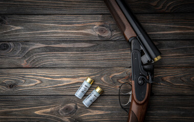 Opened double-barreled hunting rifle on a wooden table. Shotgun ammo. Dark brown wooden back.