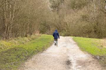 a lone man wearing a hoodie walking along a dirt track in the winter countryside  landscape orientation 